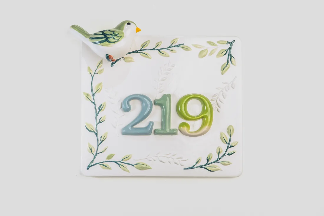 White ceramic house plaque with painted wreath, bird, and numbers 219