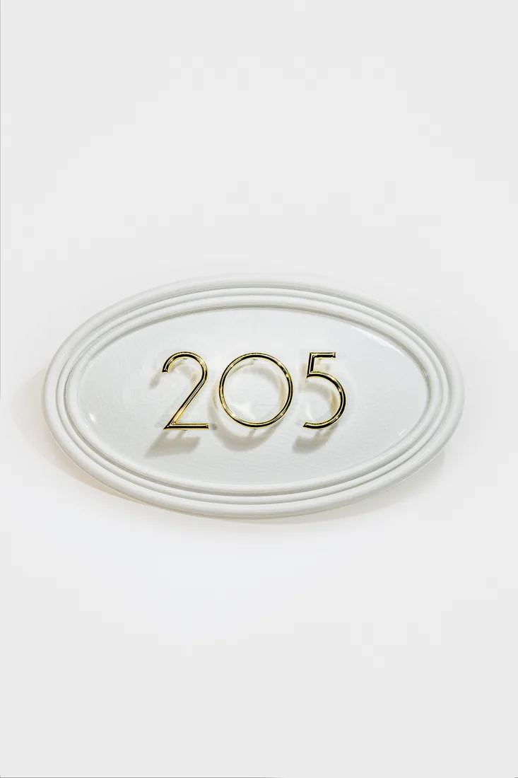 White oval address plaque with polished gold numbers 205