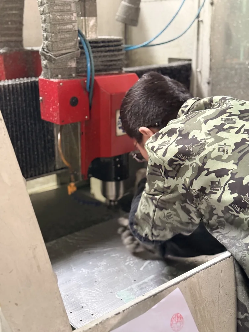 Worker checking a CNC engraving machine bed during sign production